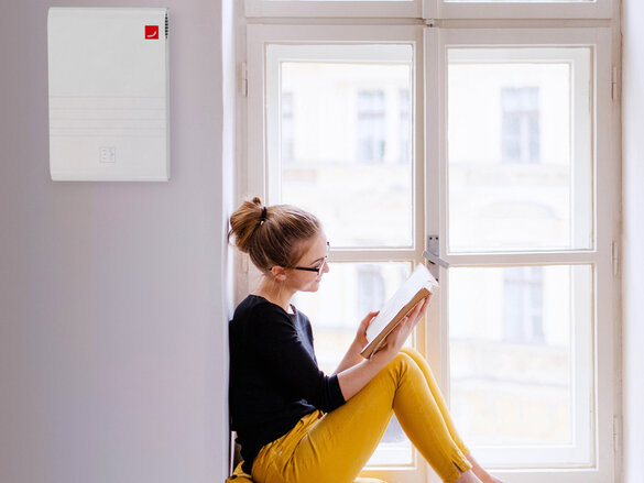 A young happy college female student with a book sitting on window sill at home, studying.